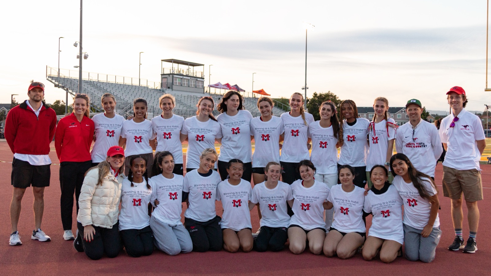 The Monte Vista girls track team in white championship shirts, with coaches at both ends.