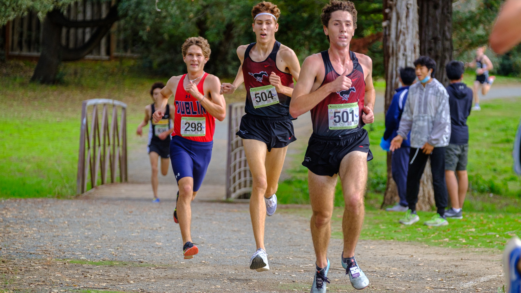 Monte Vista runners Jack Loughery and Ethan Miller racing side by side on a tree-lined cross country course.